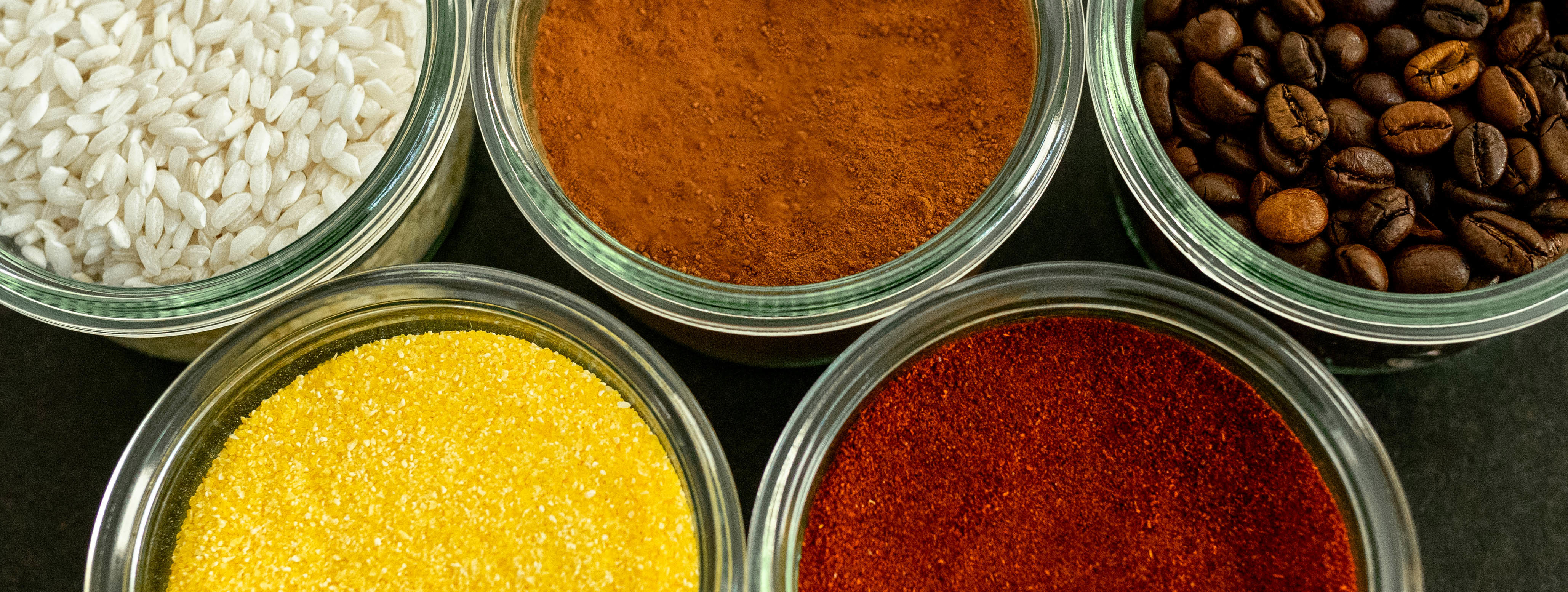 Small glass bowls of rice, cocoa, coffee beans, polenta and paprika 