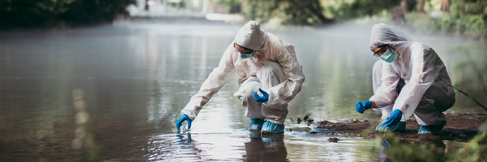 Two scientists in PPE take water samples from a river