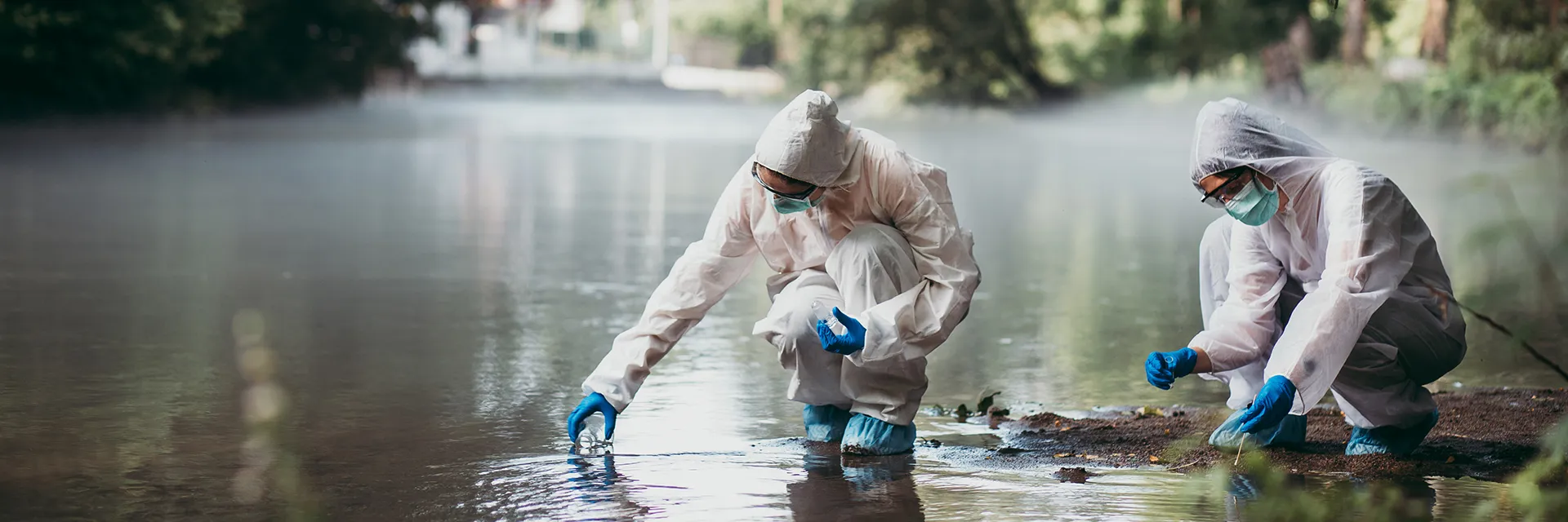 Two scientists in PPE take water samples from a river