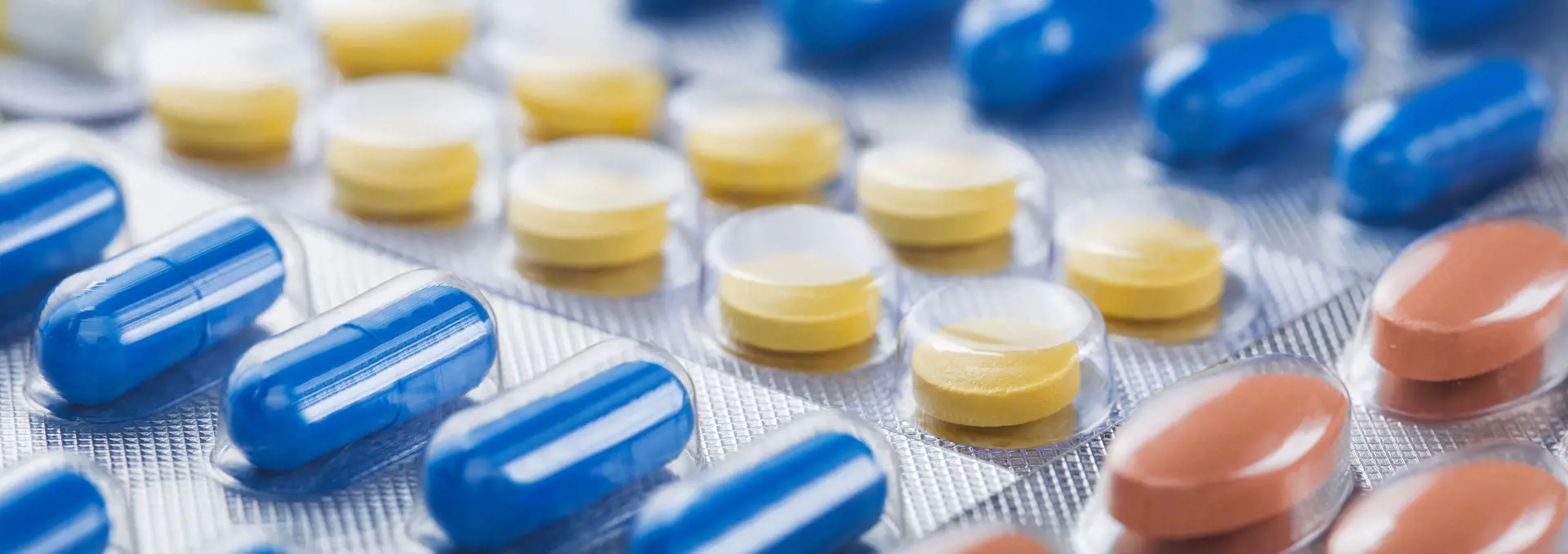 Medications in blister packaging: blue capsules, yellow tablets, brown tablets