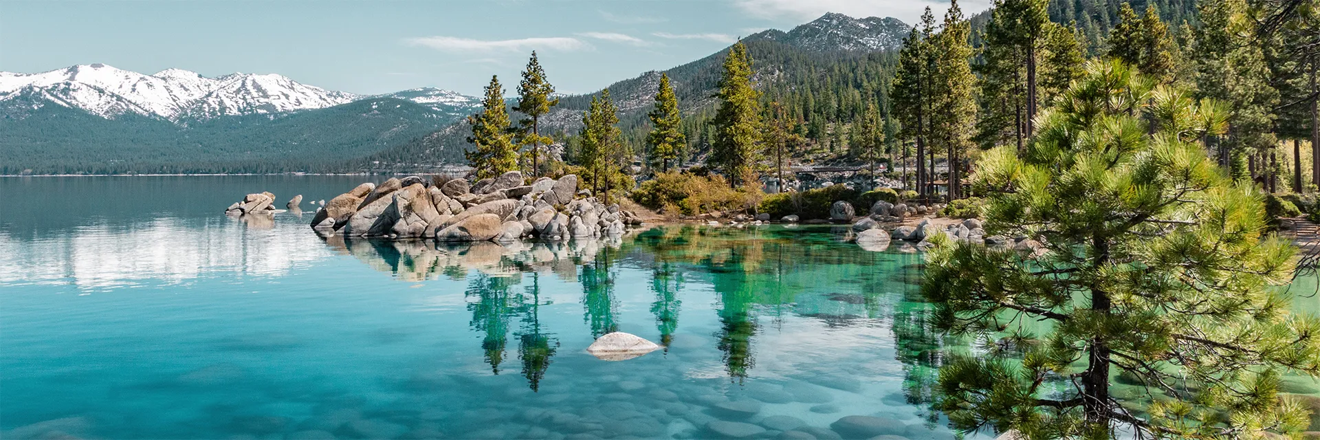 Ein blauer Bergsee mit immergrünen Bäumen und schneebedeckten Bergen im Hintergrund