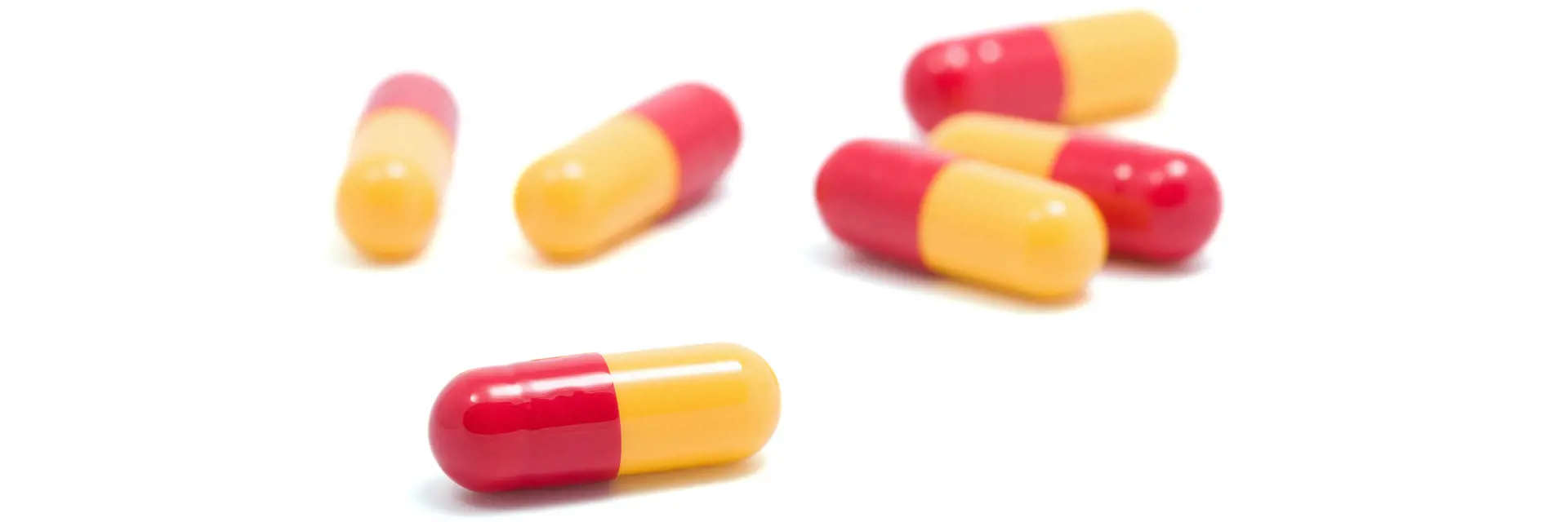 Sechs rot-gelbe Kapseln (Medikamente) auf weißem Hintergrund